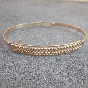 May include: A gold bangle bracelet with a double row of small beads.