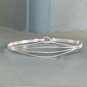 May include: A silver wire bracelet with a simple, elegant design. The bracelet is made of multiple strands of wire that are woven together to create a delicate and intricate pattern.