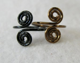 Könnte beinhalten: Zwei Drahtringe, einer schwarz und einer goldfarben, mit einem Doppelspiralen-Design.