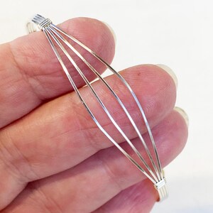 May include: A silver bangle bracelet made of five thin wires woven together. The bracelet is open and flexible.