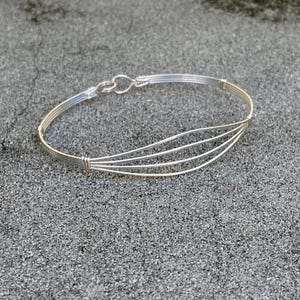 May include: A silver wire bracelet with a curved design. The bracelet is made of multiple strands of wire that are woven together.