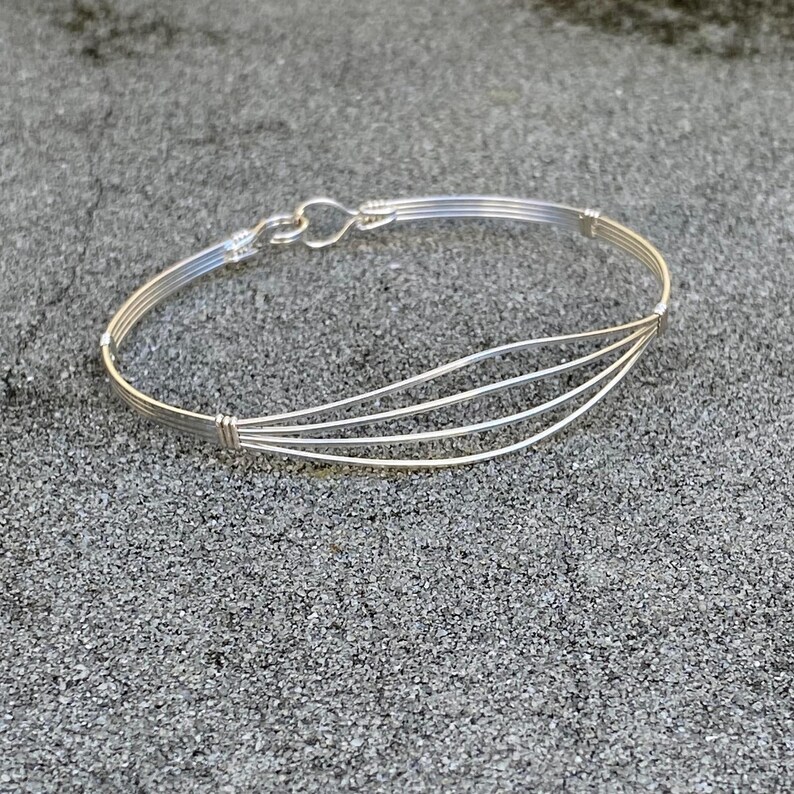 May include: A silver wire bracelet with a curved design. The bracelet is made of multiple strands of wire that are woven together.