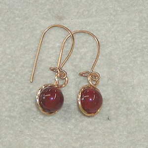 May include: A pair of gold earrings with a red glass bead on each earring.