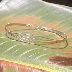 May include: A silver bangle bracelet with multiple strands of wire woven together. The bracelet is open and has a simple clasp.
