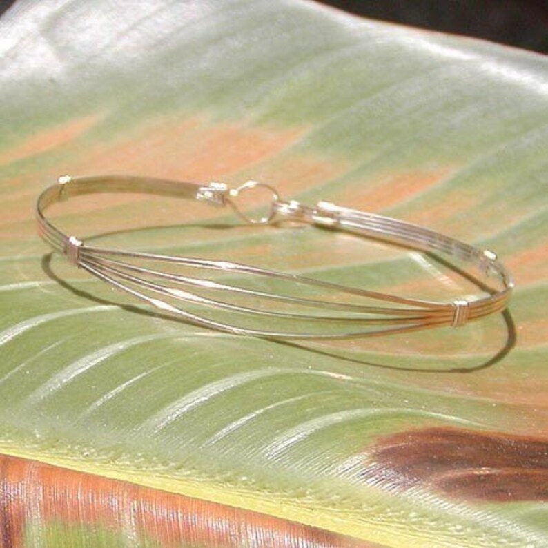 May include: A silver bangle bracelet with multiple strands of wire woven together. The bracelet is open and has a simple clasp.