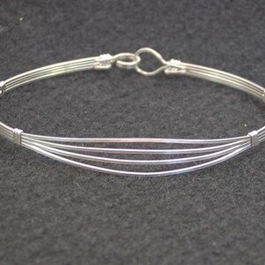 May include: A silver bangle bracelet with a simple design, featuring multiple strands of wire woven together.