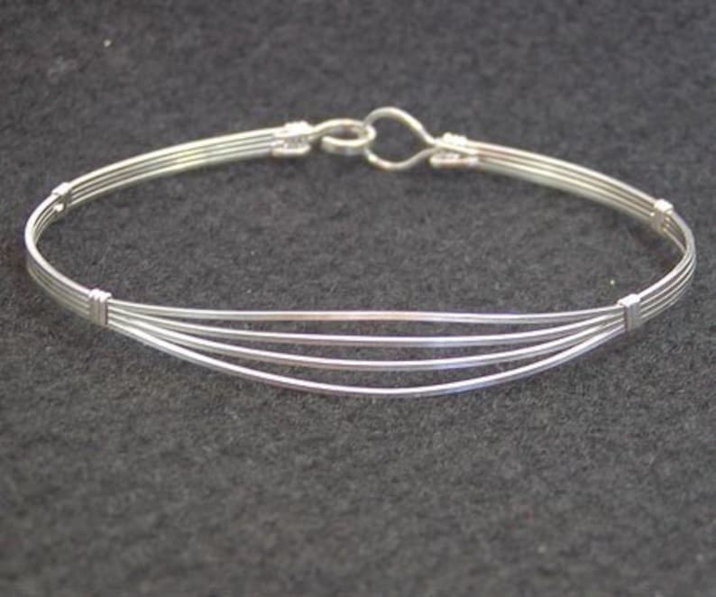 May include: A silver bangle bracelet with a simple design, featuring multiple strands of wire woven together.