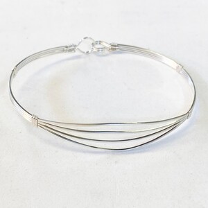 May include: A silver bangle bracelet with four strands of wire, forming a curved shape. The bracelet has a simple clasp.