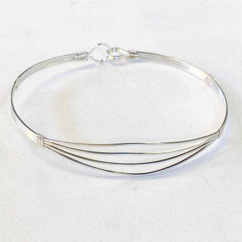 May include: A silver bangle bracelet with four strands of wire, forming a curved shape. The bracelet has a simple clasp.