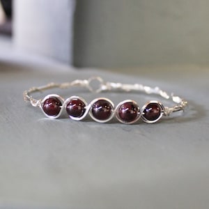May include: A silver wire bracelet with five dark red garnet beads.