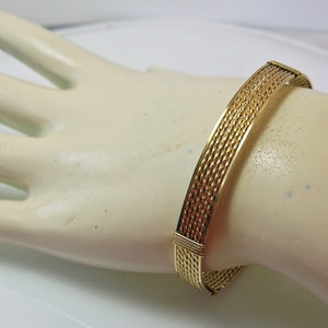 K&ouml;nnte beinhalten: Ein geflochtenes Drahtarmband in Goldton. Das Armband besteht aus mehreren Dr&auml;hten, die miteinander verflochten sind, um ein strukturiertes Muster zu erzeugen.
