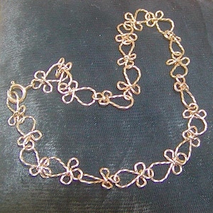 May include: A gold chain necklace with a delicate, intricate design. Each link is shaped like a small flower, creating a flowing and elegant look.