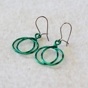 May include: A pair of green wire earrings with a double circle design. The earrings have silver hooks.