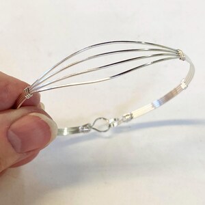 May include: A silver wire bracelet with a curved design and a clasp.