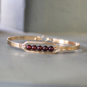 May include: A gold bangle bracelet with a rectangular frame set with six red garnet gemstones.