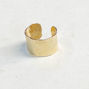 May include: A gold ear cuff with a hammered finish. The cuff is open on one side and has a slightly curved shape.