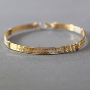 May include: A gold bangle bracelet with a braided design. The bracelet has a smooth, polished finish.