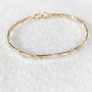 May include: A gold and silver wire bangle bracelet. The bracelet is made of two wires twisted together, one gold and one silver.