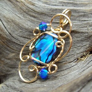 May include: A gold wire wrapped pendant featuring a blue abalone shell with iridescent colors and two blue crystal accents.