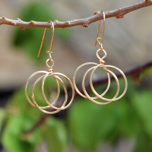 May include: Gold earrings with three interlocking circles. The earrings are hanging from a branch.