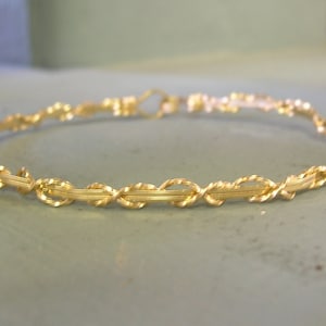 May include: A gold wire bangle bracelet with a twisted design.