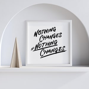 May include: A white framed print with the quote "NOTHING CHANGES IF NOTHING CHANGES" in black brush lettering. A wooden triangular ornament sits on the shelf below. The background is a white arch.