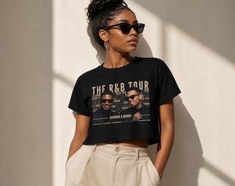 May include: Black crop top featuring the text "THE R&B TOUR" in gold lettering, with images of two men. The shirt also lists names of artists. The model is wearing sunglasses and tan pants.