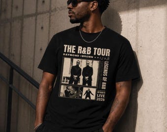 May include: Black t-shirt featuring "THE R&B TOUR" graphic with "RAYMOND BROWN" and "LEGENDS OF R&B" text. The design includes images of performers and the year "2026". The shirt is worn by a person wearing sunglasses.