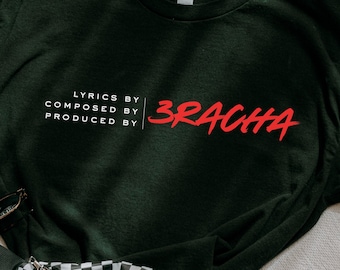 May include: Black t-shirt with white text that reads "Lyrics by, Composed by, Produced by" and red text that reads "3racha".