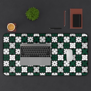 May include: A rectangular desk mat featuring a green, white, and black floral design. A laptop, mouse, pen, notebook, and a coffee cup are on the mat. The mat covers a large portion of the desk surface.