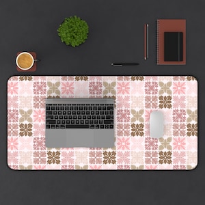 May include: A rectangular desk mat with a floral tile pattern in shades of pink, brown, and white. A laptop, mouse, pen, notebook, and a small plant are on the mat. A cup of coffee sits on a coaster.