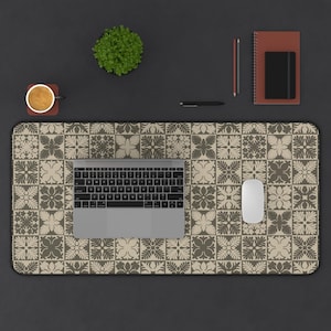May include: A rectangular desk mat featuring a repeating tile pattern in shades of beige and dark brown. The mat is placed on a dark surface with a silver laptop, a white computer mouse, a coffee mug, a small potted plant, and a notebook.