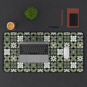 May include: A black and green patterned desk mat with a laptop and a white mouse on top. The desk mat has a geometric design with green and white flowers.