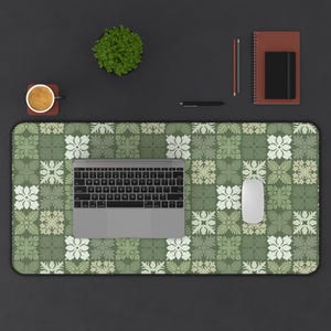 May include: A green and white floral patterned desk mat with a laptop, mouse, and keyboard. A small potted plant, a cup of coffee, a pen, a pencil, and a notebook are also on the desk.
