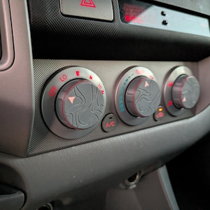 May include: Close-up of a car's dashboard with three silver knobs. The knobs have red markings and are labelled "OFF", "LO", "HI", "A/C", and "REC".