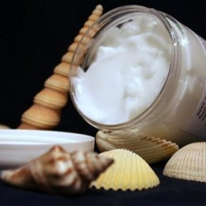 May include: A white jar of deep conditioner cream with a seashell theme. The jar is open and the cream is visible. The jar is surrounded by seashells.