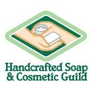 May include: A green diamond-shaped logo with the text "Handcrafted Soap & Cosmetic Guild" in white. The logo features a hand holding a small jar of cream and a bar of soap.