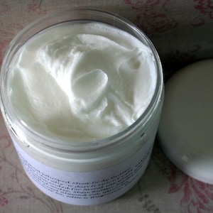 May include: A white jar of body butter with a white lid. The jar is labeled with the text "Whipped Shea Body Butter" and a list of ingredients.