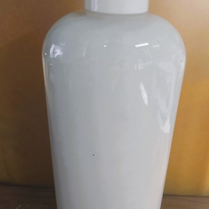 May include: A white ceramic bottle with a white lid. The bottle is smooth and has a rounded shape.