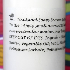 May include: White bottle with black text that reads "Toadstool Soaps Shower Gel". The text continues with instructions on how to use the product and a list of ingredients: "To use: Apply small amount to run in circular motion over body. KEEP OUT OF EYES. Ingred. - Olive Butter, Vegetable Oil, Vit E, Aloe, Potassium Sorbate, Potassium"