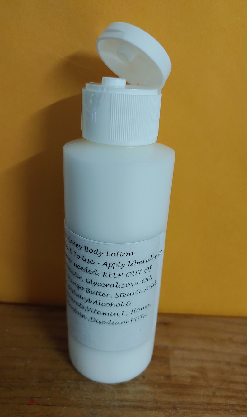 May include: A white plastic bottle of honey body lotion with a white flip top lid. The bottle is labeled with the text "Honey Body Lotion" and instructions for use. The ingredients are listed as: Water, Glyceral, Soya Oil, Mango Butter, Stearic Acid, Cetyl Alcohol, Honey, Vitamin E, Disodium EDTA.