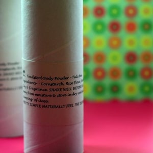 May include: White cardboard tube with a black label that reads "Toadstool Body Powder - Talc free" and lists the ingredients: cornstarch, rice flour, and fragrance. The label also instructs to shake well before use, keep away from moisture, and store in a dry container. The label also says "Pretty Simple Naturally Feel The Difference".