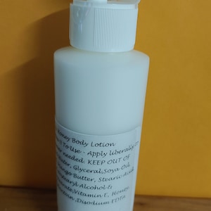 May include: A white plastic bottle of honey body lotion with a white flip top lid. The bottle is labeled with the text "Honey Body Lotion" and instructions for use. The ingredients are listed as: Water, Glyceral, Soya Oil, Mango Butter, Stearic Acid, Cetyl Alcohol, Honey, Vitamin E, Disodium EDTA.