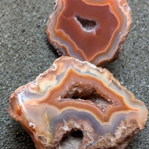 Op de afbeelding: Twee agaatplakken met bruine, oranje en witte banden. De agaatplakken hebben een natuurlijke, ruwe rand en een gat in het midden.