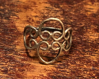 Puede incluir: Un anillo de plata con un diseño delicado e intrincado de círculos y óvalos superpuestos. El anillo está hecho de un metal fino y tiene un estilo simple y elegante.