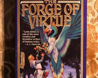 May include: A blue book cover with gold lettering that reads "The Forge of Virtue" by Lynn Abbey. The cover features an illustration of a white bird with blue and green feathers, a man in armour, and a sword. The book is part of the Ultima Saga series.