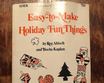 May include: A vintage book cover with the title "Easy-to-Make Holiday Fun Things" by Roz Abisch and Boche Kaplan. The cover features illustrations of various holiday symbols, including a Christmas tree, a dreidel, a turkey, a shamrock, an Easter egg, a witch, a dragon, and a totem pole.