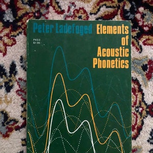 May include: A green book titled "Elements of Acoustic Phonetics" by Peter Ladefoged. The cover features a graphic of sound waves in blue, yellow, and white.