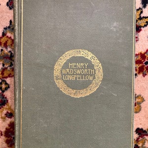Puede incluir: Un libro de tapa dura verde con letras doradas en la portada. El título dice "HENRY WADSWORTH LONGFELLOW".