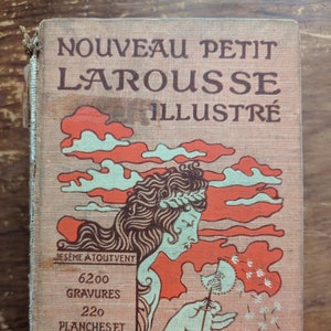 Op de afbeelding: Een vintage boekomslag met de titel "Nouveau Petit Larousse Illustre" in een decoratief lettertype. De omslag toont een illustratie van een vrouw met lang bruin haar die op een paardenbloem blaast. De tekst "Je seme a tout vent" is onder de illustratie gedrukt. De boekomslag is in tinten rood, oranje en wit.